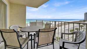 A balcony with a table and chairs, overlooking a beach and ocean.