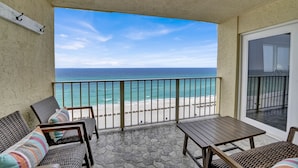 A balcony with wicker furniture, a stone floor, and a view of the beach and ocean.