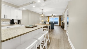 A modern kitchen with white cabinetry, a granite countertop, and a bar area with stools.