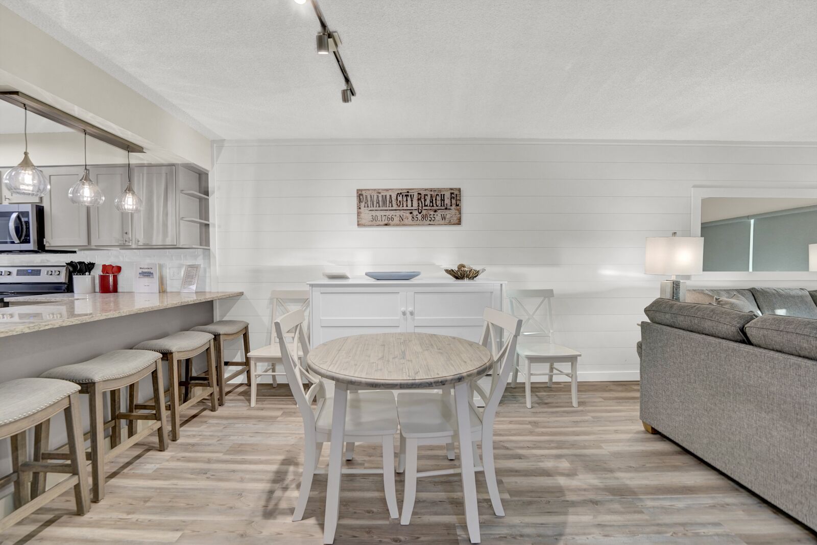 A modern kitchen with white cabinetry, a central island with stools, and a dining table with chairs. There is a sign on the wall indicating the location.