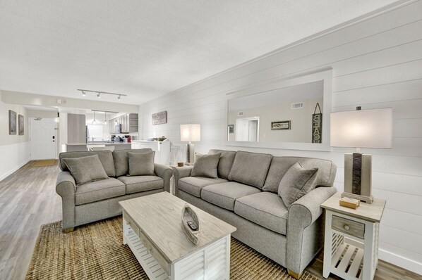 A modern living room with two grey sofas, a wooden coffee table, and a side table with a lamp.