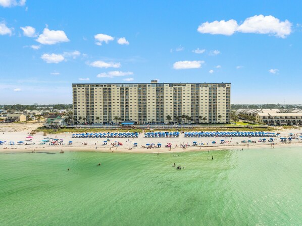 Un hotel grande con varios pisos, una playa al frente y numerosas sombrillas en la arena.