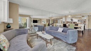 A spacious living area with a grey sofa, a coffee table, and a dining area with chairs and a table.