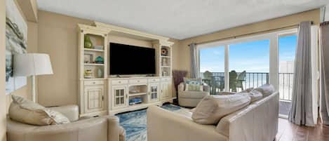 Amplia sala de estar con un televisor de pantalla plana grande, mobiliario blanco y vistas de la ciudad a través de amplios ventanales.