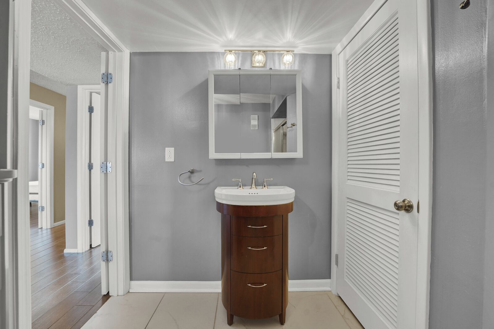 Un baño con tocador, espejo y tres luces sobre el espejo.