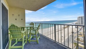 A balcony with green Adirondack chairs and a table, overlooking a beach with a clear sky.