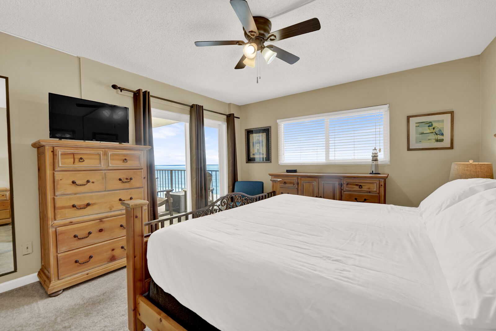 A bedroom with a bed, dresser, television, and a balcony with a view.