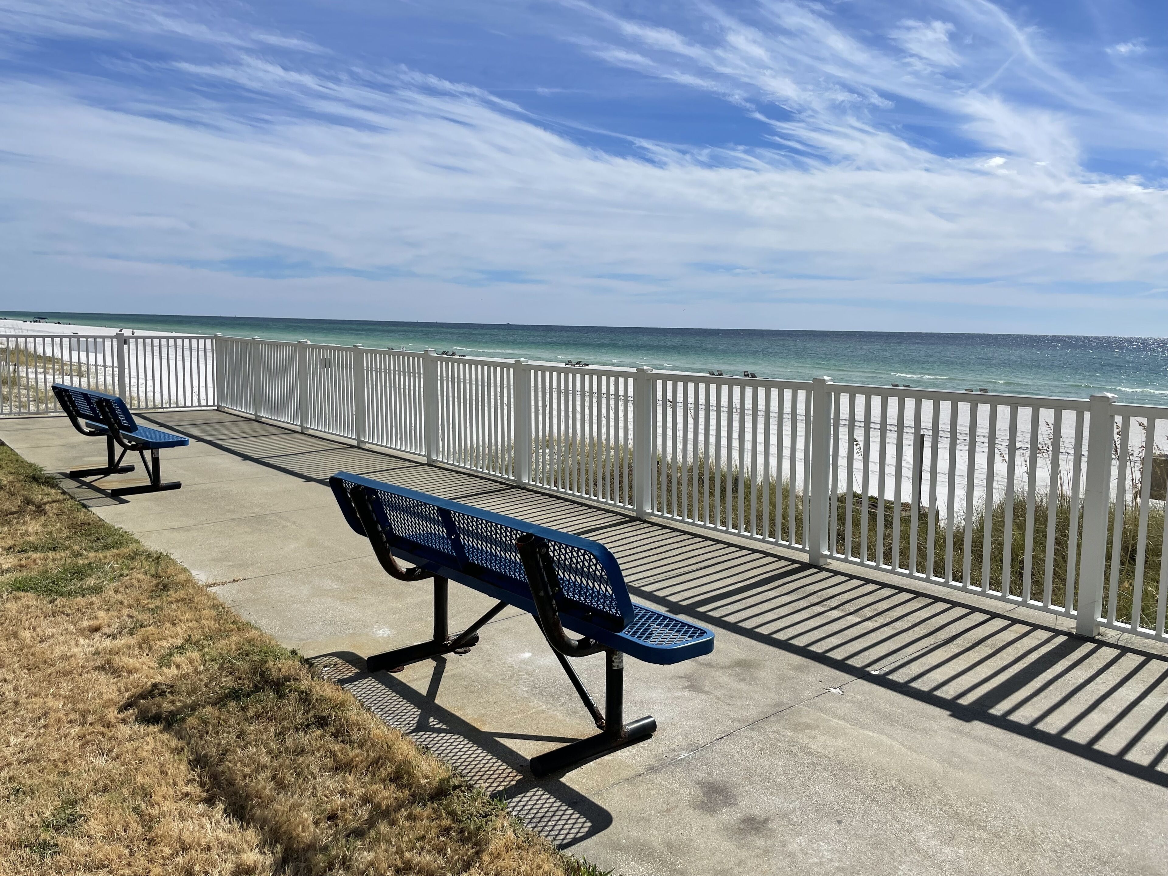 A concrete walkway with two blue benches overlooking a beach.
