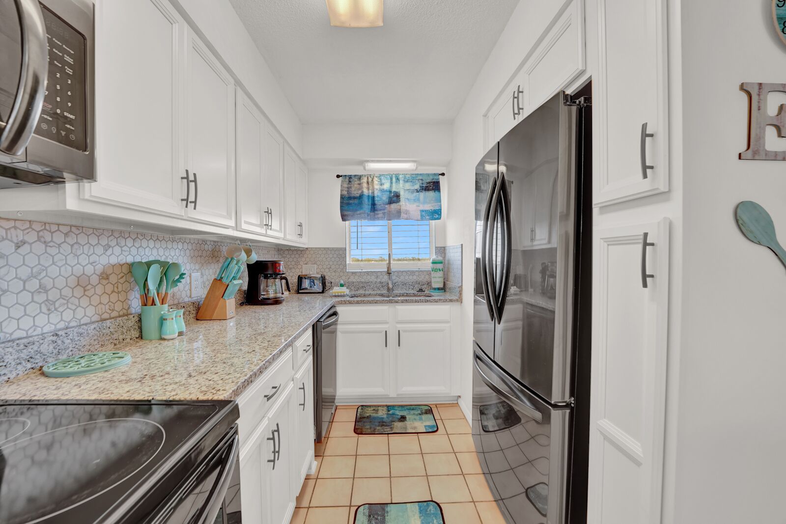 A modern kitchen with white cabinets, stainless steel appliances, and a window with a view.