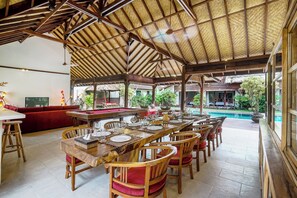 A dining area with a pool view, wooden furniture, and a thatched roof. - Large 5 bedroom villa with big pool - Seminyak (Seminyak)