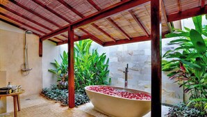A bathroom with a freestanding bathtub filled with rose petals, surrounded by lush greenery and a wooden ceiling structure. - Large 5 bedroom villa with big pool - Seminyak (Seminyak)