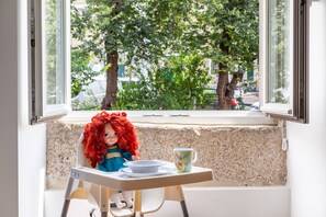A doll in a high chair by a window with a view of trees and buildings. - By the Castle | STYLISH AND SPACIOUS | Family-Friendly (Lisboa)
