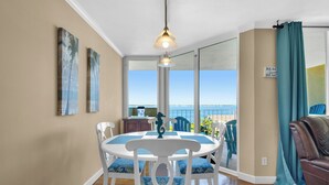 Un comedor con una mesa y sillas blancas, una lámpara colgante y vista al océano a través de amplios ventanales.