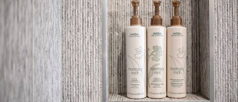Drei Flaschen Aveda Rosmarin-Minze-Shampoo und -Spülung auf einem strukturierten, hellen Fliesenregal.