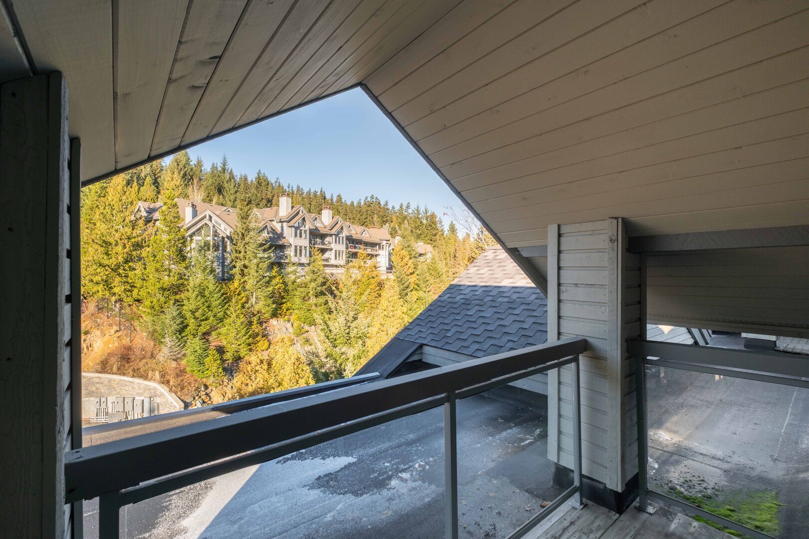 A view from a balcony with a large window overlooking a forested area and a multi-story building.