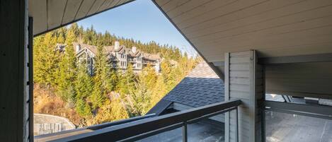 A view from a balcony with a large window overlooking a forested area and a multi-story building.