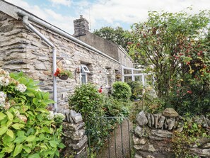 A stone house with a stone wall, a window, and a hanging flower basket. - Cwm Caeth Cottage (Caernarfon)