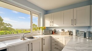 A modern kitchen with white cabinets, a large window, and a view of greenery. - Stylish Family-Friendly Sea-View Home, sleeps 9 (Tenby)
