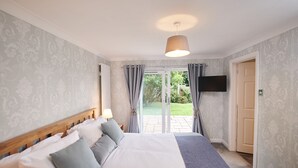 A bedroom with a large bed, a TV mounted on the wall, and a sliding glass door leading to an outdoor area. - Stylish Family-Friendly Sea-View Home, sleeps 9 (Tenby)