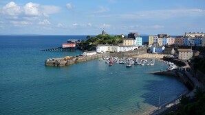 A coastal town with a harbor, colorful buildings, and a prominent hill with a structure on top. - Stylish Family-Friendly Sea-View Home, sleeps 9 (Tenby)