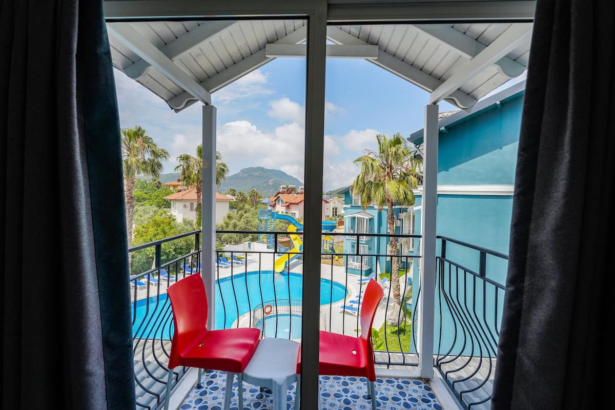 A balcony with a pool view, red chairs, and a table.