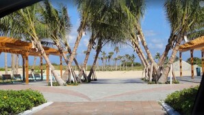 A covered outdoor area with palm trees, benches, and a paved walkway leading to a beach. - Professional 2 Bedroom Condo on Singer Island, FL.  FREE parking.  Beach 5 min. (Singer Island)