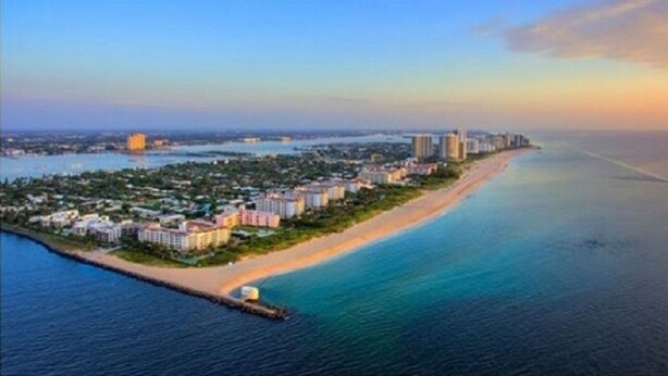 An aerial view of a coastal resort with beachfront properties, a marina, and a city skyline in the distance. - Professional 2 Bedroom Condo on Singer Island, FL.  FREE parking.  Beach 5 min. (Singer Island)