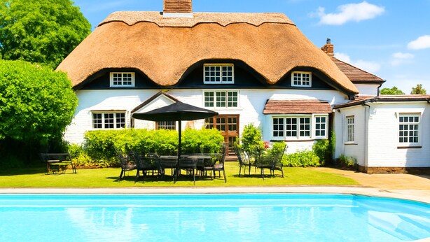 Una casa con techo de paja, piscina, mobiliario exterior y césped cuidado.