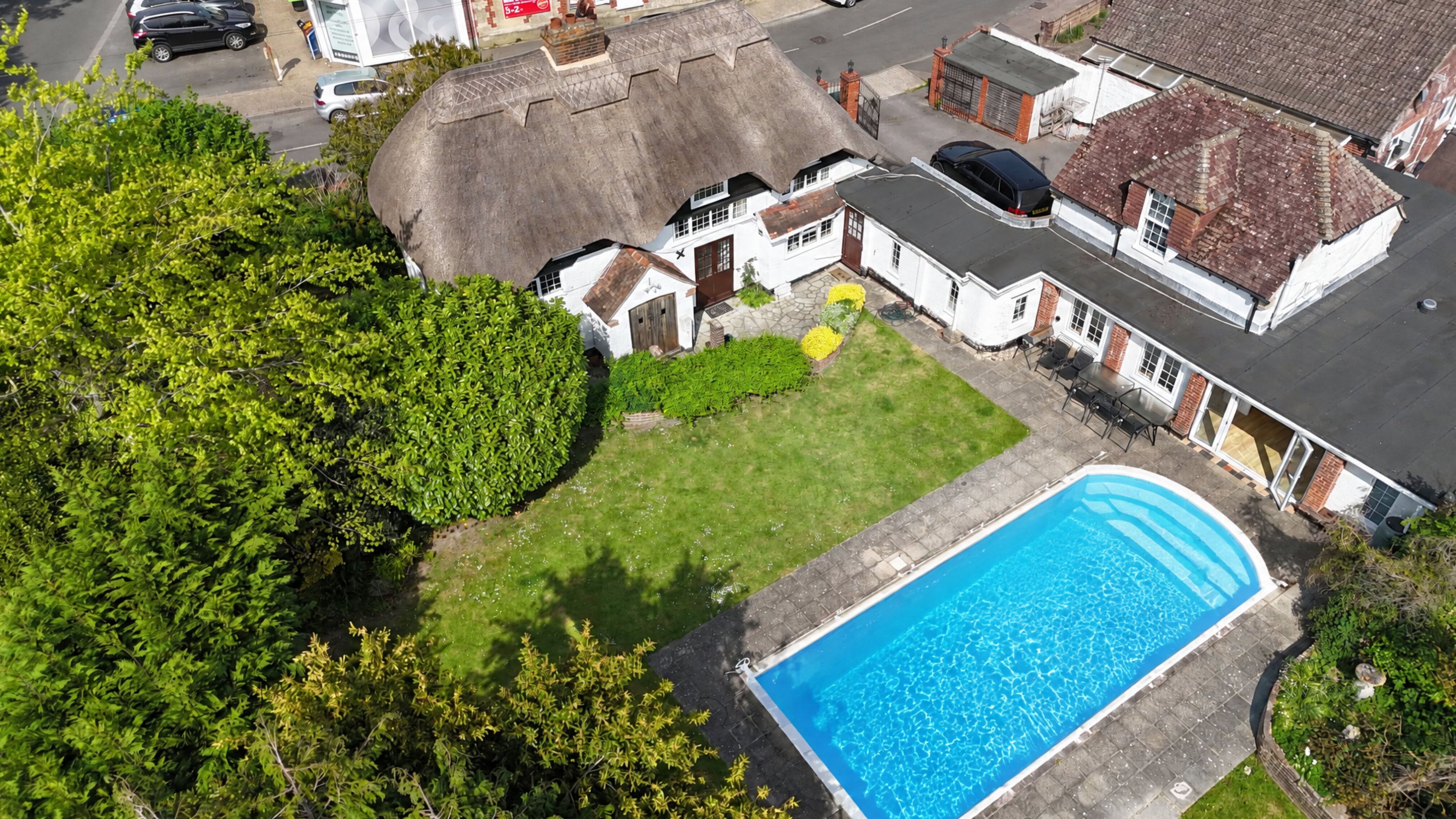 Um imóvel residencial com piscina, casa com telhado de palha e gramado bem cuidado.