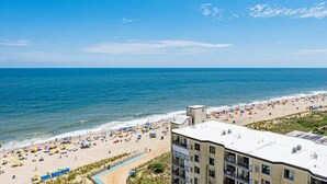 A beach view with a building in the foreground. - 9400 Building - Oceanfront Condo with Panoramic views of the ocean and bay! (Ocean City)