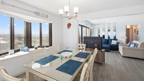 A modern living room with a glass dining table, a flat-screen TV, and a sofa. - 9400 Building - Oceanfront Condo with Panoramic views of the ocean and bay! (Ocean City)