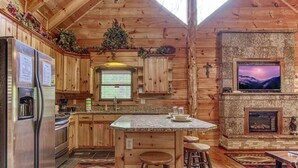Eine gemütliche Küchenzeile im Blockhausstil mit Holzwänden, einer Arbeitsplatte aus Granit und einem Kamin aus Stein.
