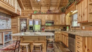 Eine rustikale Küche mit Holzschränken, einer Granit Arbeitsplatte, einem Side-by-Side Kühlschrank, einer Mikrowelle und einem Geschirrspüler.