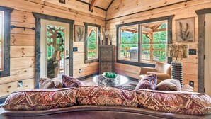A cozy log cabin interior with a curved sofa, a ceiling fan, and large windows offering a view of the outdoors. - Red Cedar Lodge #396 (Sevierville)