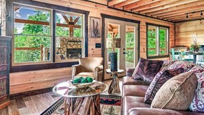A cozy cabin interior with a stone fireplace, wooden beams, a leather sofa, and large windows offering a view of the outdoors. - Red Cedar Lodge #396 (Sevierville)