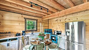 A modern kitchen with wooden walls, stainless steel appliances, and a dining area with green chairs. - Red Cedar Lodge #396 (Sevierville)