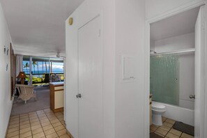 Ein Zimmer mit Blick auf Palmen und das Meer, eine weiße Tür, ein Badezimmer mit türkisfarbener Duschvorhang und ein gefliestes Badezimmer.