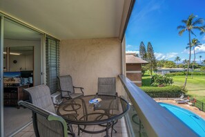 Ein Balkon mit Glastisch und Stühlen, der auf einen Swimmingpool und eine üppige Landschaft mit Palmen blickt.