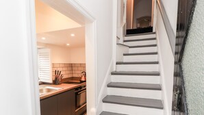 Una scala conduce a una cucina dal design moderno, con lavello in acciaio inossidabile, bollitore e piano di lavoro con utensili da cucina.