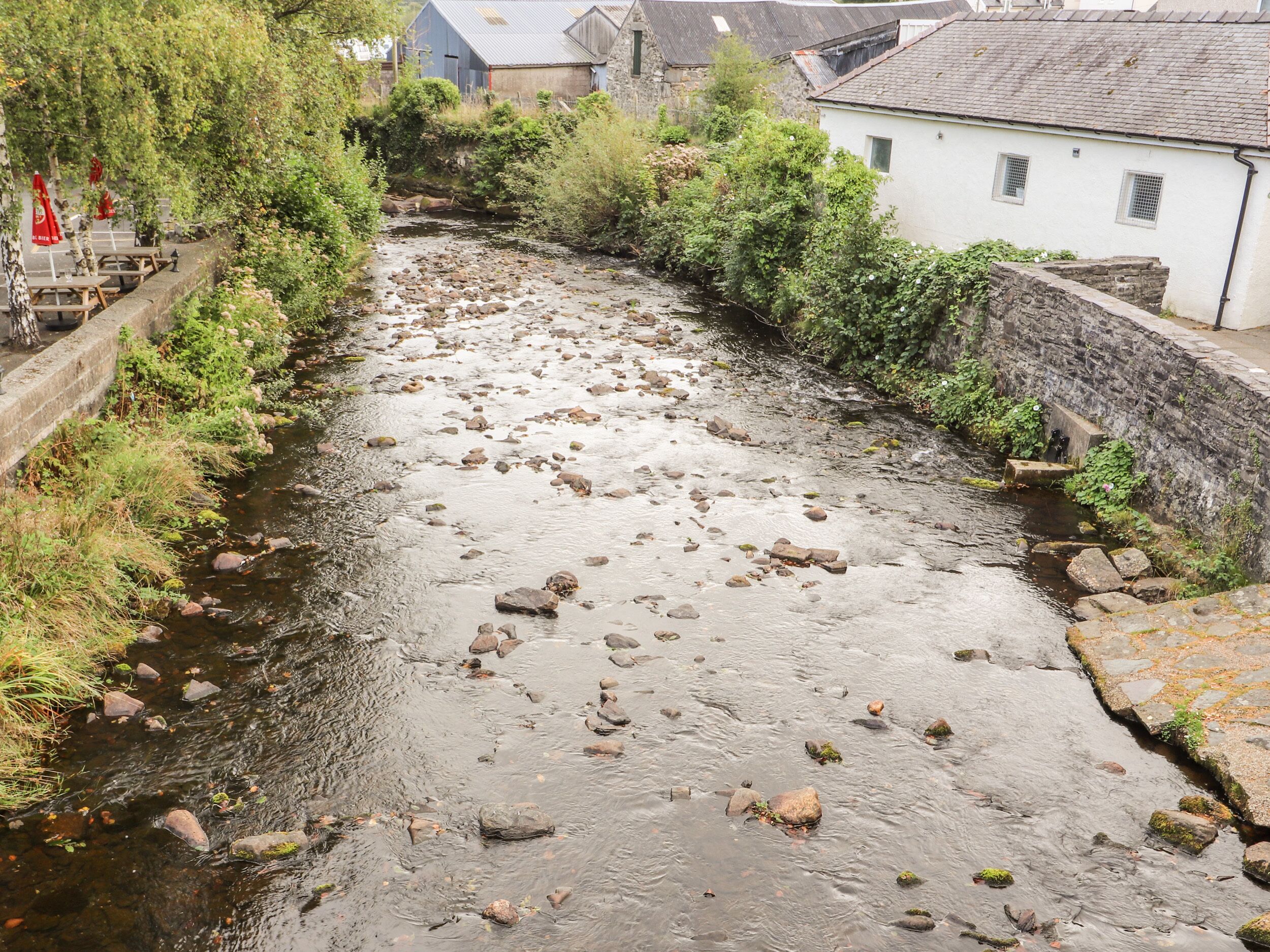 A narrow river with rocks and greenery on both sides, surrounded by stone walls and buildings.