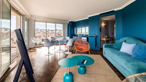 Ein modernes Wohnzimmer mit großem Fenster, einem Türkis-farbenen Sofa und einem Essbereich mit Stühlen und Tisch.