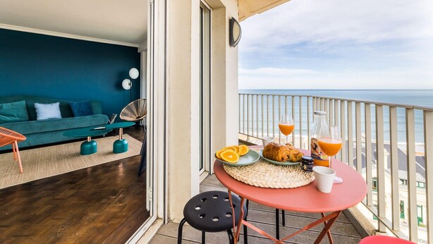 Ein Balkon mit Frühstückstisch, einer Couch und Blick auf das Meer.