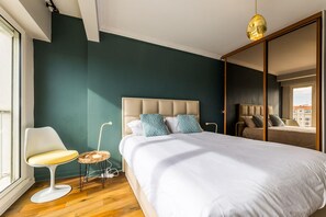 Um quarto moderno com uma cama grande, uma mesa de cabeceira, uma cadeira e uma janela.
