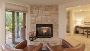 A living room with a stone fireplace, leather chairs, and a view through a glass door to an outdoor area.