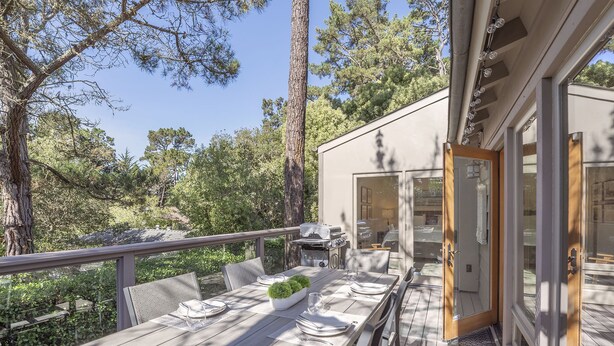 An outdoor dining area with a wooden deck, a grill, and a view of the surrounding forest.
