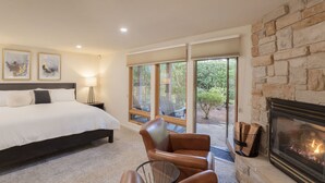 A bedroom with a large bed, a fireplace, a stone wall, and a view of the outdoors.