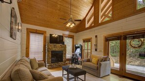 L’intérieur chaleureux d’un chalet avec une cheminée en pierre, un plafond en bois et de grandes fenêtres.