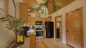 Une cuisine rustique, située dans une cabane en bois, avec un îlot central, des meubles en bois, un réfrigérateur noir et une plante en pot.
