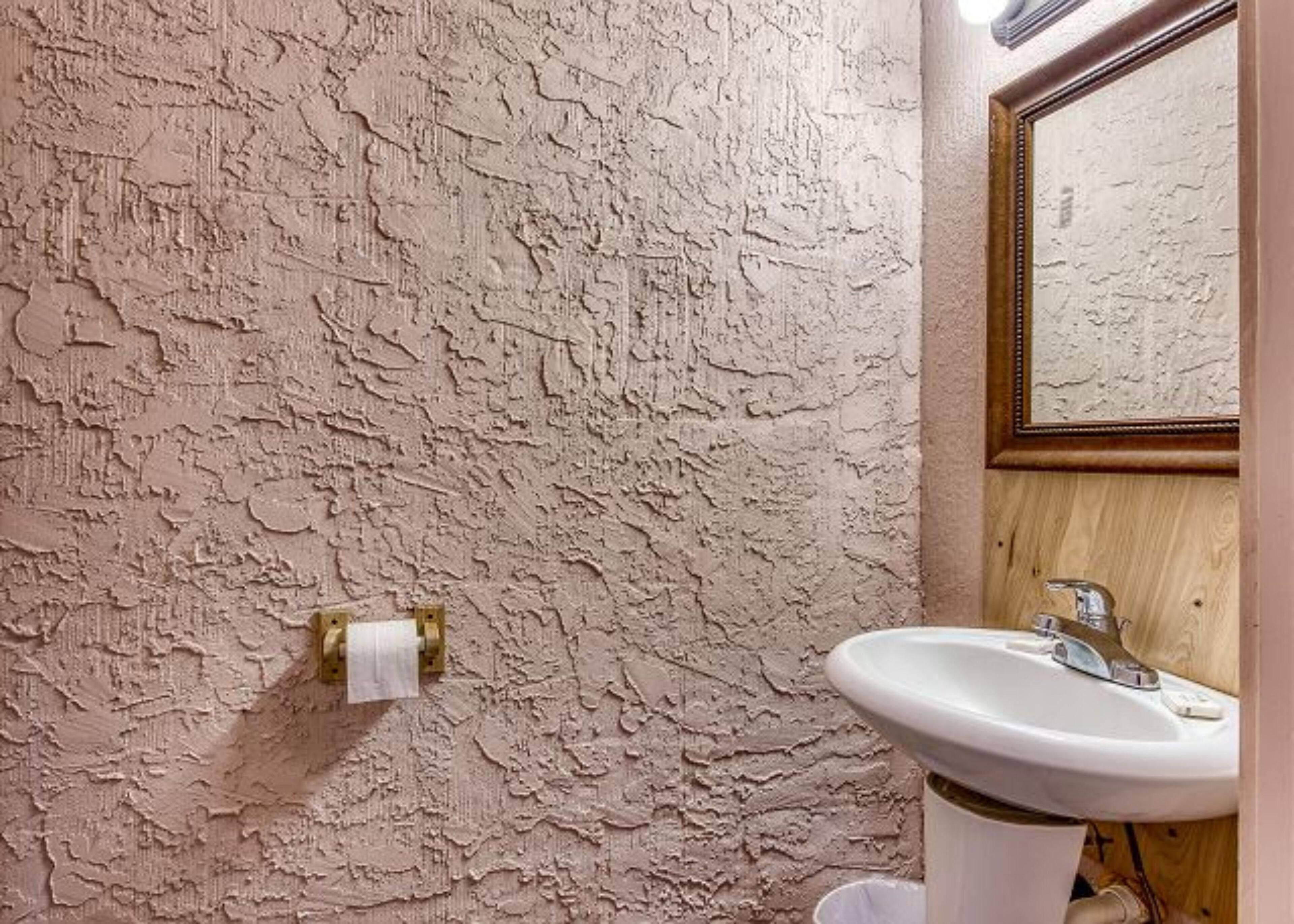 Ein Badezimmer mit strukturierter Wand, einem weißen Waschbecken und einem Holzkorpus.