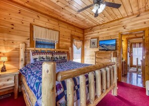 A wooden cabin bedroom with a bed, a ceiling fan, a TV, and a window with curtains. - Bear Foot Lodge #308 (Sevierville)